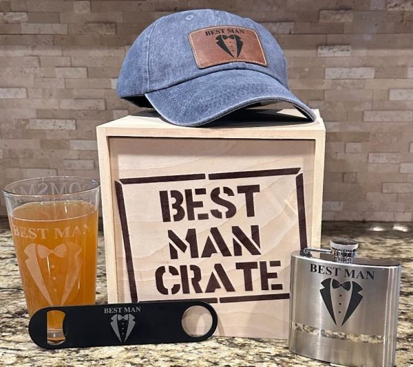 A display of Best Man themed items includes a crate labeled "Best Man Crate" containing four items: a blue distressed hat with a "Best Man" logo, a beer glass with "Best Man" on it, a black bottle opener featuring the same logo, and a metallic flask also labeled "Best Man.