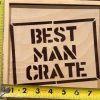 A wooden box with the words "Best Man Crate" stenciled in black. Yellow measuring tapes are placed around the box, showing its dimensions: approximately 10.75 inches in width and 9.5 inches in height. Inside, you'll find carefully selected Best Man items from the Best Man Crate with 4 Best Man Items including a blue distressed hat perfect for any occasion.