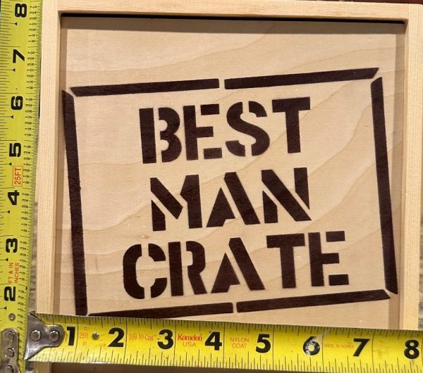 A wooden box with the words "Best Man Crate" stenciled in black. Yellow measuring tapes are placed around the box, showing its dimensions: approximately 10.75 inches in width and 9.5 inches in height. Inside, you'll find carefully selected Best Man items from the Best Man Crate with 4 Best Man Items including a blue distressed hat perfect for any occasion.