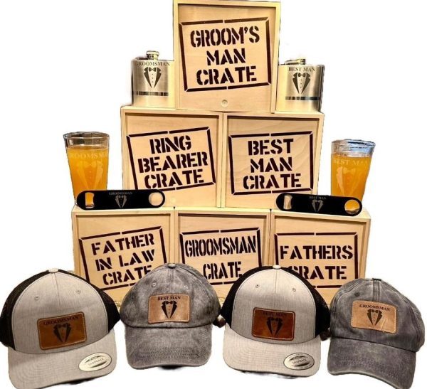 A display of wooden crates labeled "Groom Man Crate," "Ring Bearer Crate," "Best Man Crate," and "Father in Law Crate." Each Groom Man Crate - Wooden Gift Box includes a flask, caps with emblems, a pint glass, and a bottle opener.