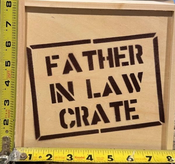 The "Father In Law Crate - Wooden Gift Box" features the words "Father in Law Crate" stenciled on the lid in black paint. The crate's dimensions are highlighted by yellow tape measures placed along its left and bottom sides, making it an ideal gift for your father-in-law.