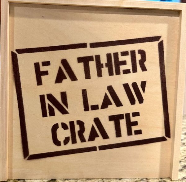 The image showcases a charming "Father In Law Crate - Wooden Gift Box" sitting on a countertop. A close-up of the front of the wooden crate highlights the bold, uppercase letters stenciled with the words "FATHER IN LAW CRATE.