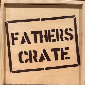 The Fathers Crate - Wooden Gift Box features the words "FATHERS CRATE" prominently stenciled in bold black letters on the front, enclosed within a rectangular border. The crate is crafted from light-colored wood and boasts a simple, rustic design, making it an ideal gift for Dad.