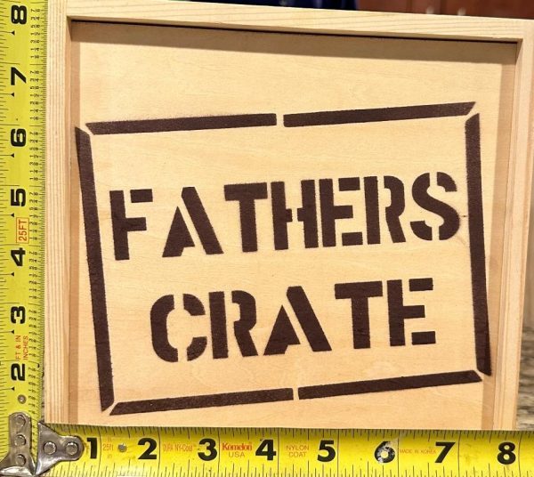 A Fathers Crate - Wooden Gift Box is seen with yellow measuring tapes placed vertically and horizontally next to it. The crate appears to be approximately 10 inches tall and 15 inches wide, based on the measurements shown by the tapes.