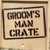 A Groom Man Crate - Wooden Gift Box with the text "GROOM'S MAN CRATE" stenciled in bold, black letters on the front. The crate features a natural wood finish and is displayed on a speckled surface.