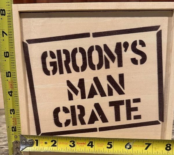 A product labeled "Groom Man Crate - Wooden Gift Box" is showcased with two yellow measuring tapes positioned across it. One tape measures the height, showing approximately 9 inches, and the other measures the width, showing about 12 inches.