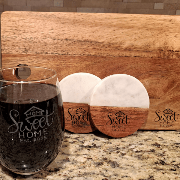 Two rectangular marble coasters with wooden accents. Each coaster has the phrase "Home Sweet Home Est. 2024" engraved on the wooden part. The design includes a small house icon atop the text.